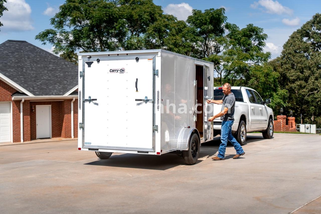 Reboque comercial fechado acoplado a uma caminhonete em frente a um centro de distribuição, ilustrando uma solução para ampliar a capacidade de transporte de encomendas.