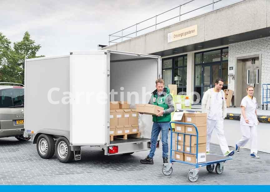 Caixas de papelão organizadas no compartimento de carga de um reboque fechado, com as portas traseiras abertas para facilitar o acesso durante o carregamento.
