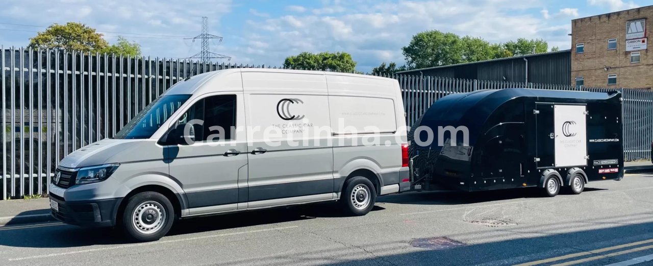 Uma van compacta de carga e um reboque baú estacionados lado a lado em um centro de distribuição, representando duas alternativas para operações de entrega.