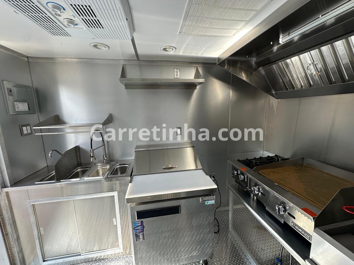 Interior de um trailer de alimentação com bancadas, equipamentos comerciais, refrigeração e pia organizados para aproveitar o espaço disponível.