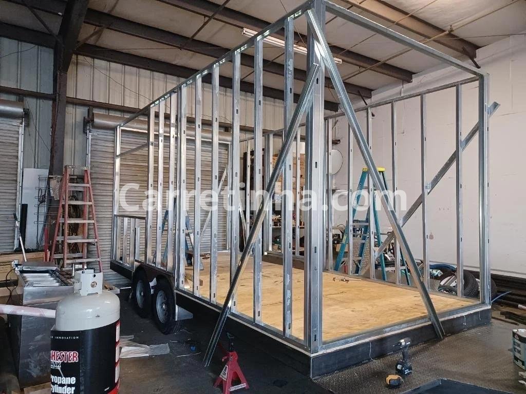 Estrutura metálica de um trailer comercial em fase de fabricação, com destaque para o chassi, os eixos e os componentes de rodagem.