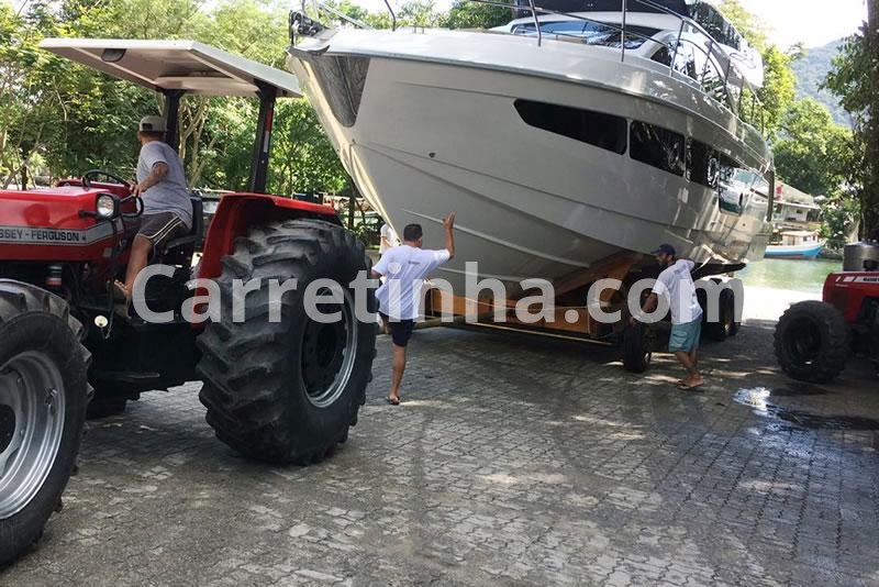 Operador conduzindo um trator especializado para movimentar uma embarcação apoiada em carreta náutica dentro da marina.